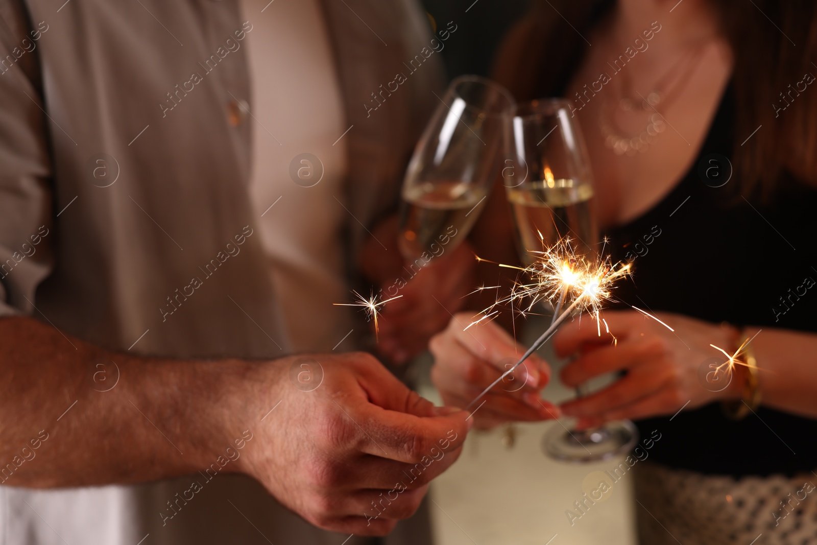 Photo of Friends celebrating New Year with sparklers and wine glasses indoors, closeup
