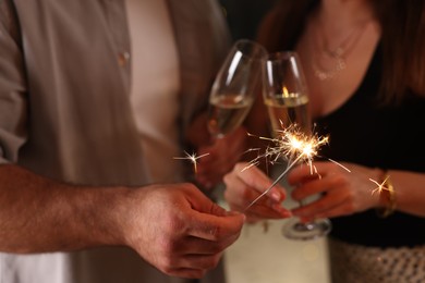 Photo of Friends celebrating New Year with sparklers and wine glasses indoors, closeup