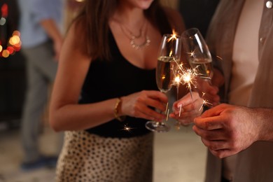 Photo of Friends celebrating New Year with sparklers and wine glasses indoors, closeup