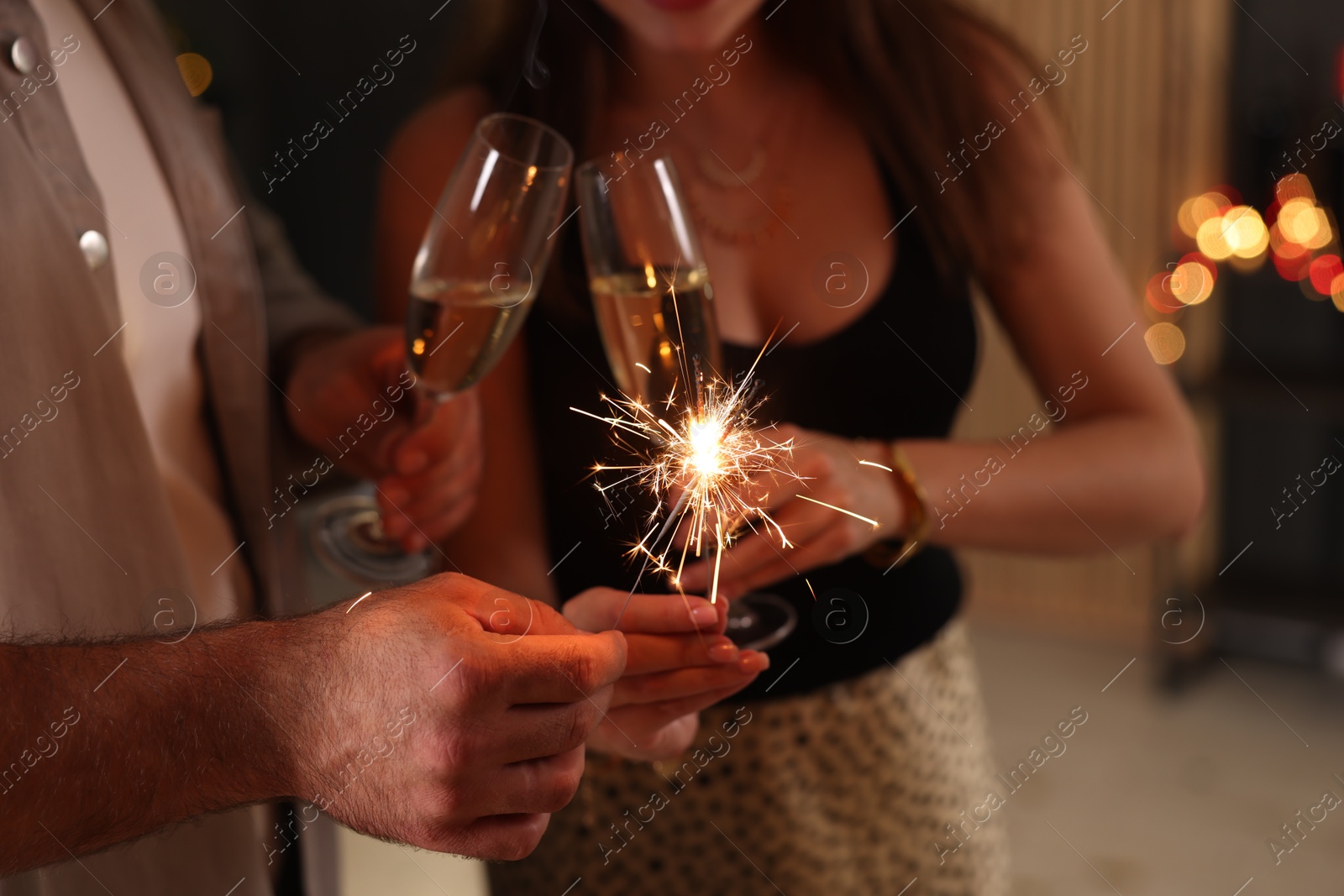 Photo of Friends celebrating New Year with sparklers and wine glasses indoors, closeup