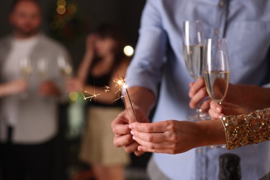Photo of Friends celebrating New Year with sparklers and wine glasses indoors, closeup