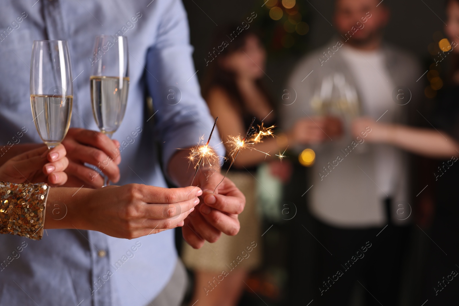 Photo of Friends celebrating New Year with sparklers and wine glasses indoors, closeup