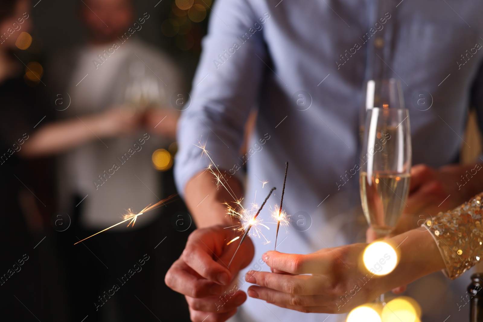 Photo of Friends celebrating New Year with sparklers and wine glasses indoors, closeup