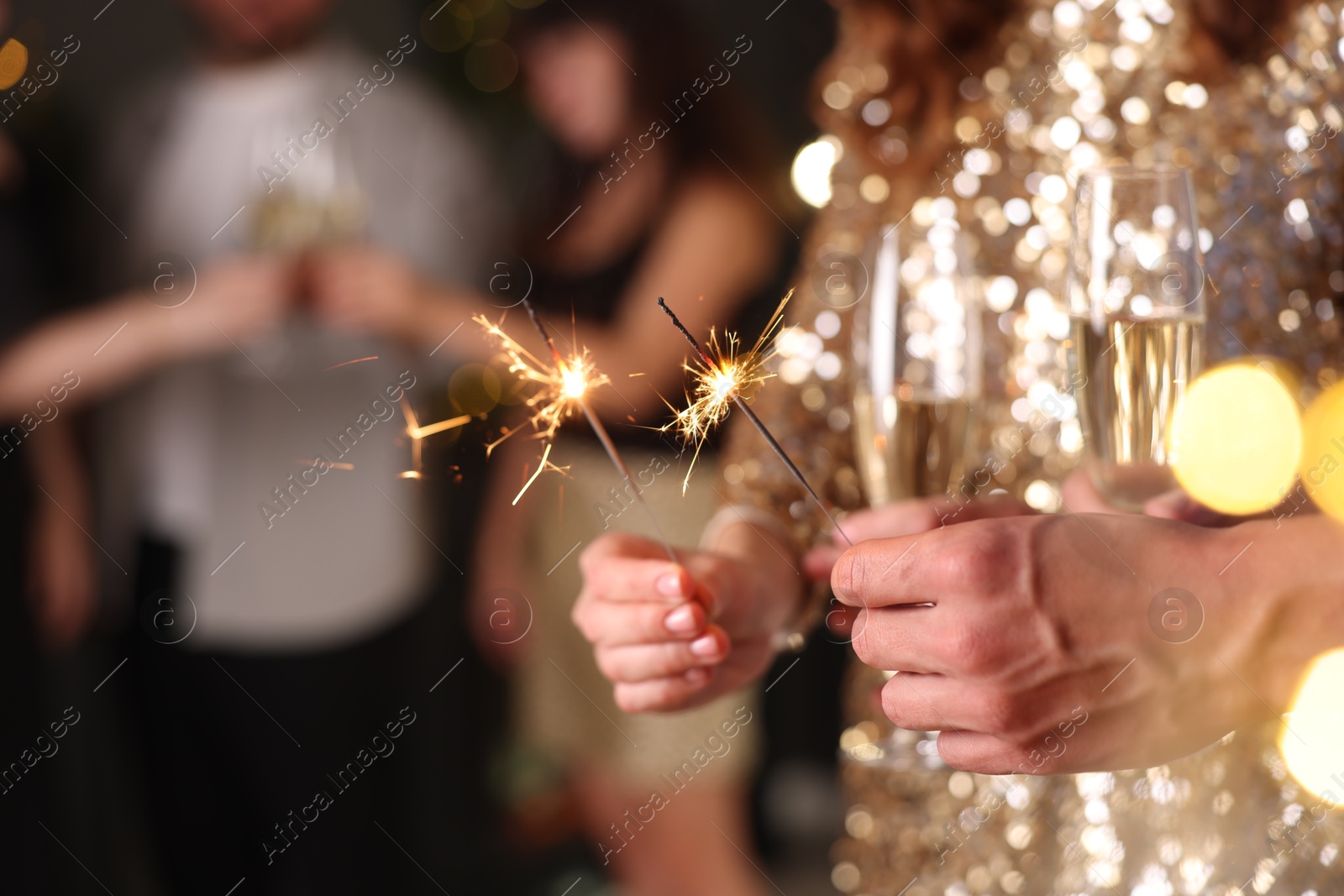 Photo of Friends celebrating New Year with sparklers and wine glasses indoors, closeup