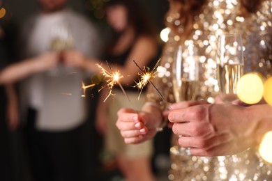 Photo of Friends celebrating New Year with sparklers and wine glasses indoors, closeup