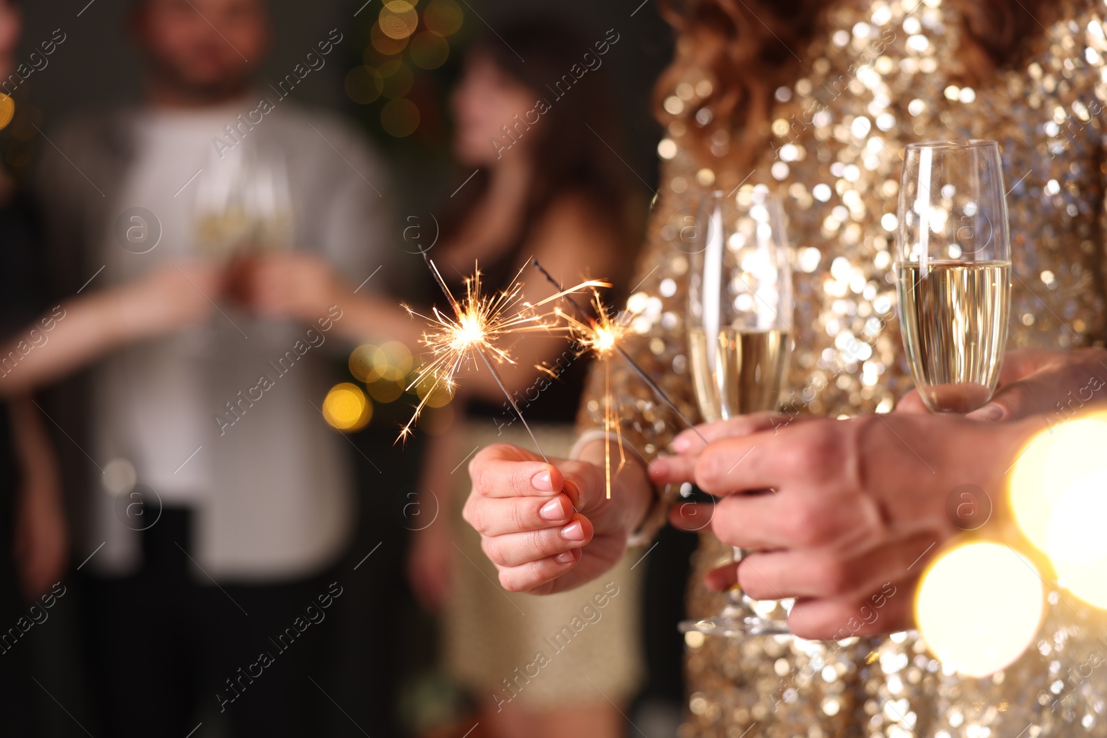 Photo of Friends celebrating New Year with sparklers and wine glasses indoors, closeup