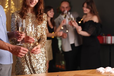 Photo of Friends celebrating New Year with sparklers and wine glasses indoors, closeup