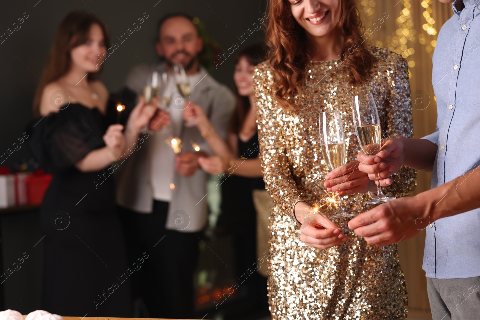 Photo of Friends celebrating New Year with sparklers and wine glasses indoors, closeup