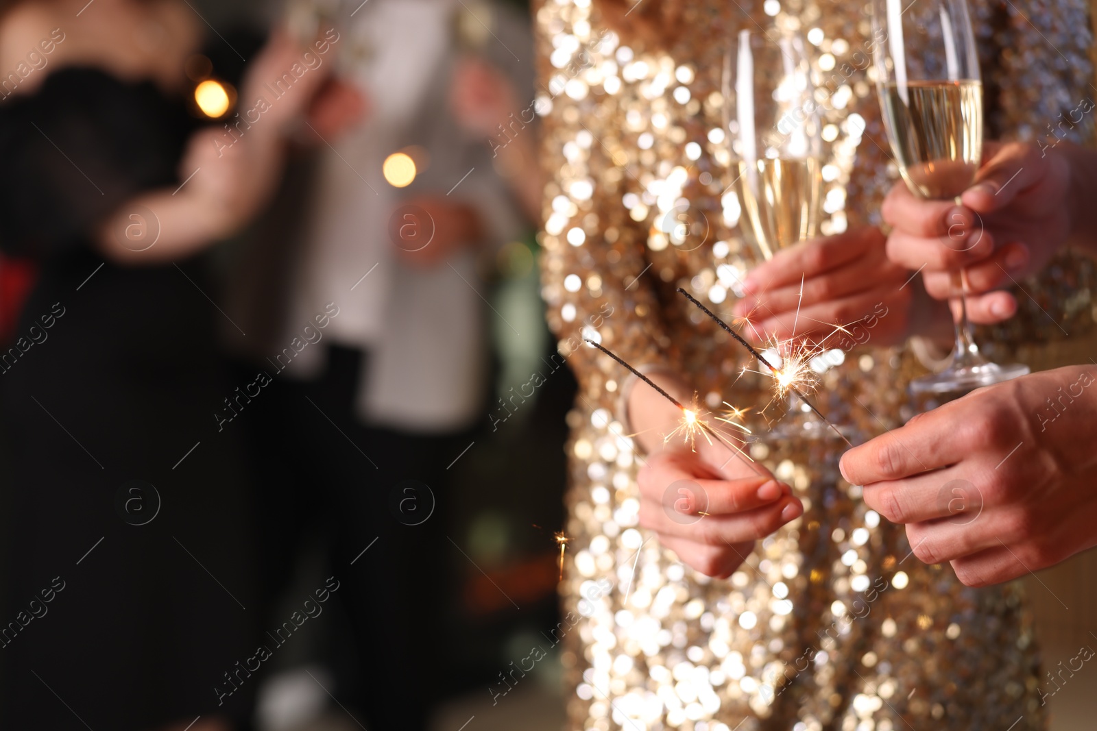 Photo of Friends celebrating New Year with sparklers and wine glasses indoors, closeup