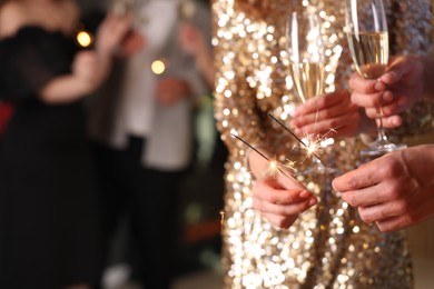 Photo of Friends celebrating New Year with sparklers and wine glasses indoors, closeup