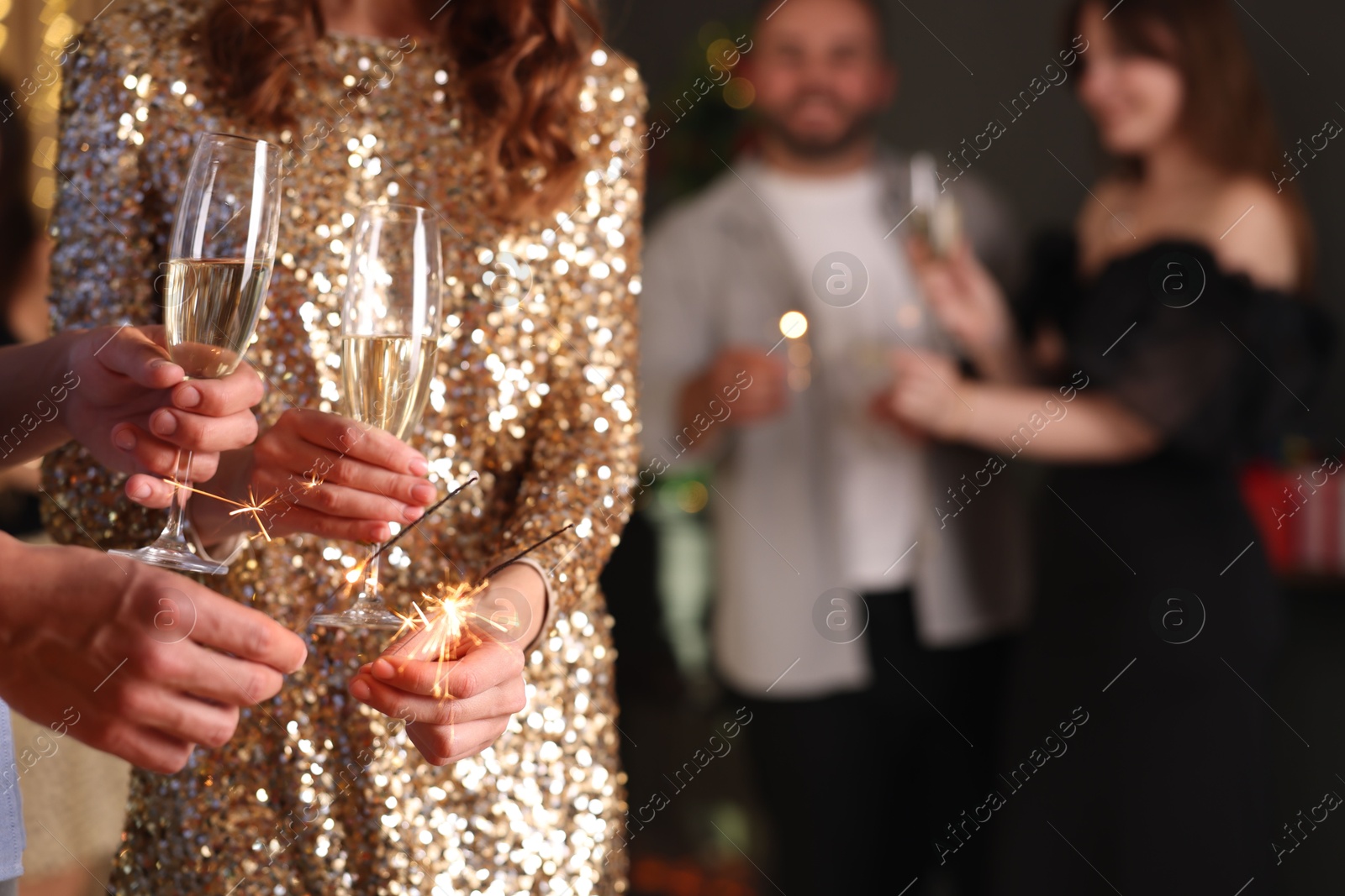 Photo of Friends celebrating New Year with sparklers and wine glasses indoors, closeup
