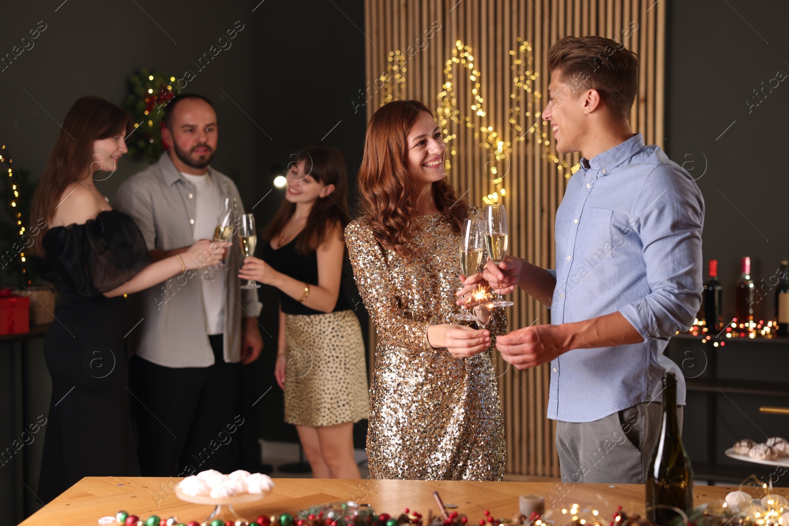 Photo of Friends celebrating New Year with sparklers and wine glasses indoors