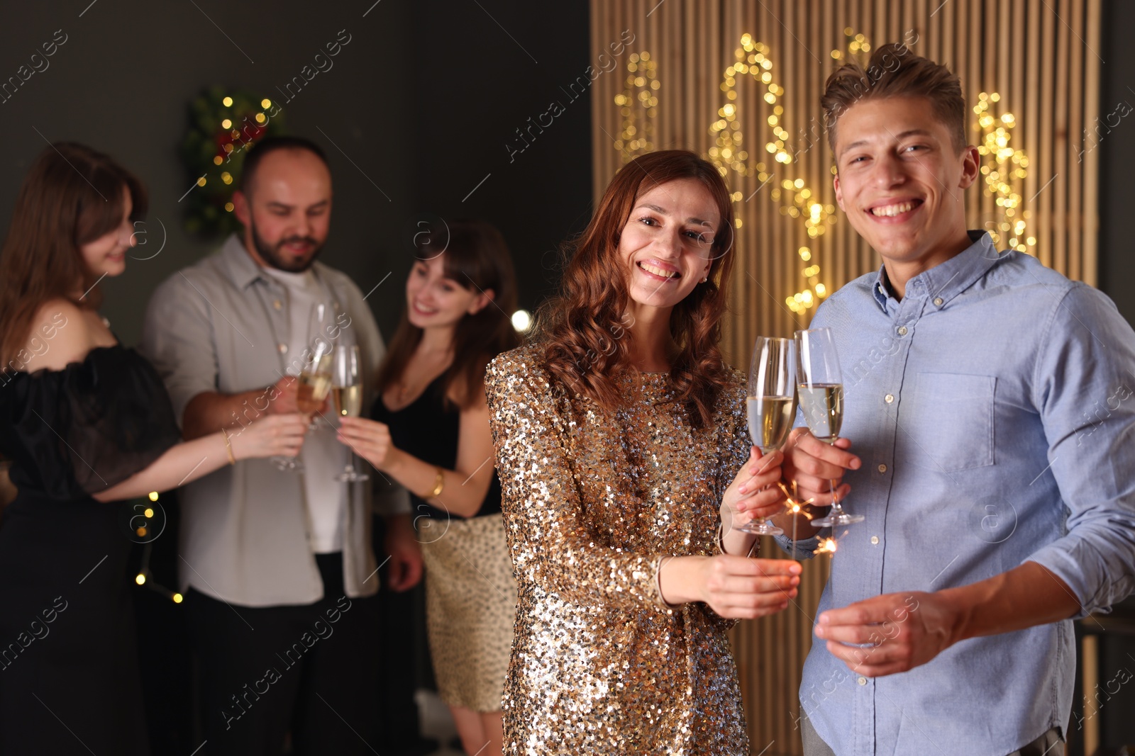 Photo of Friends celebrating New Year with sparklers and wine glasses indoors