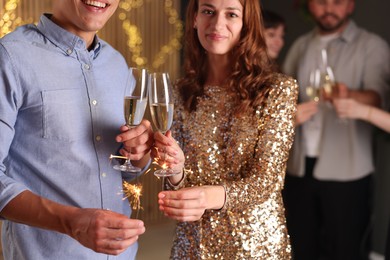 Photo of Friends celebrating New Year with sparklers and wine glasses indoors, selective focus