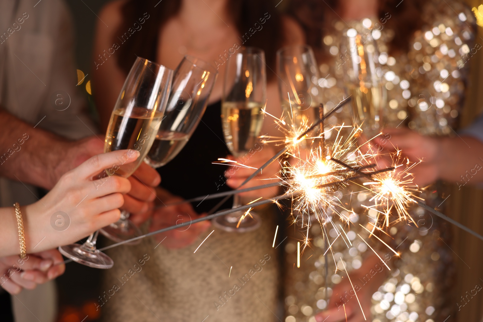 Photo of Friends celebrating New Year with sparklers and wine glasses indoors, closeup