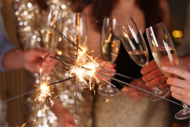 Photo of Friends celebrating New Year with sparklers and wine glasses indoors, closeup