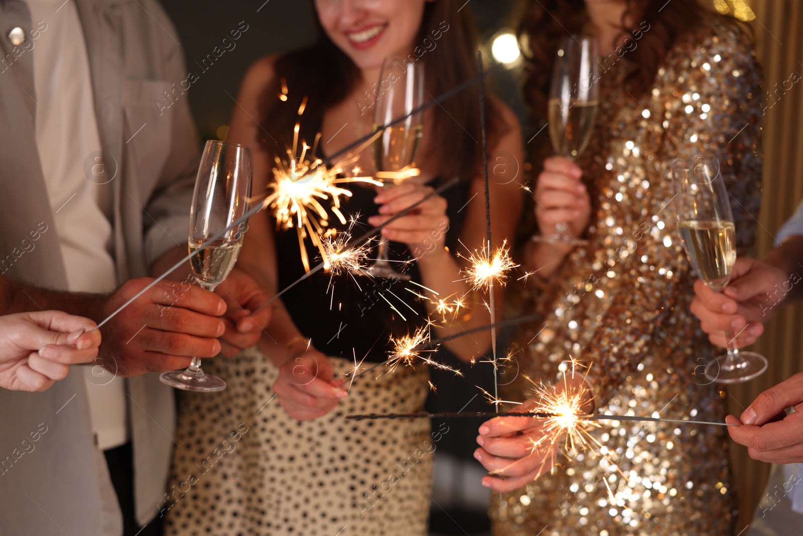 Photo of Friends celebrating New Year with sparklers and wine glasses indoors, closeup