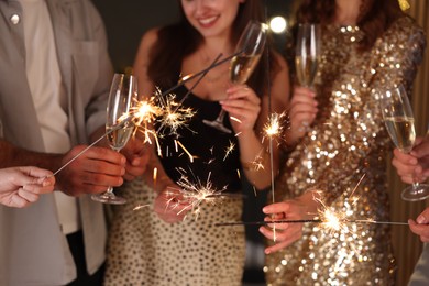 Photo of Friends celebrating New Year with sparklers and wine glasses indoors, closeup