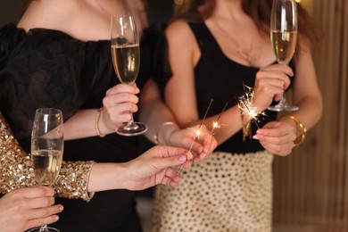 Photo of Women celebrating New Year with sparklers and wine glasses indoors, closeup