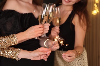 Photo of Women celebrating New Year with sparklers and wine glasses indoors, closeup