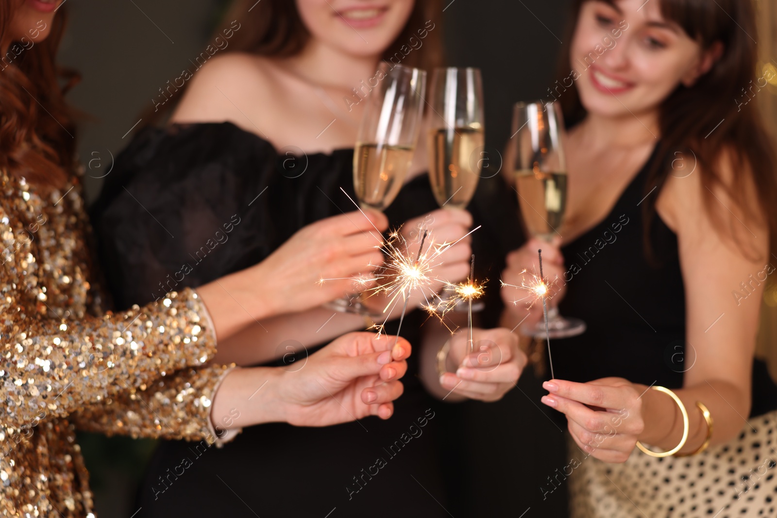 Photo of Women celebrating New Year with sparklers and wine glasses indoors, closeup