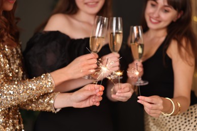 Photo of Women celebrating New Year with sparklers and wine glasses indoors, closeup