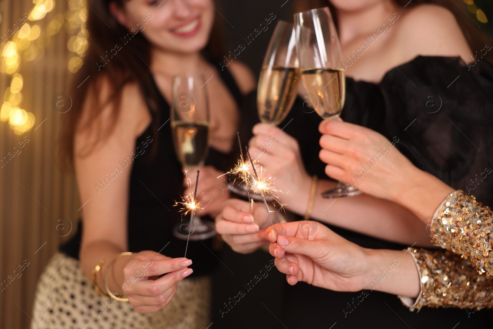 Photo of Women celebrating New Year with sparklers and wine glasses indoors, closeup