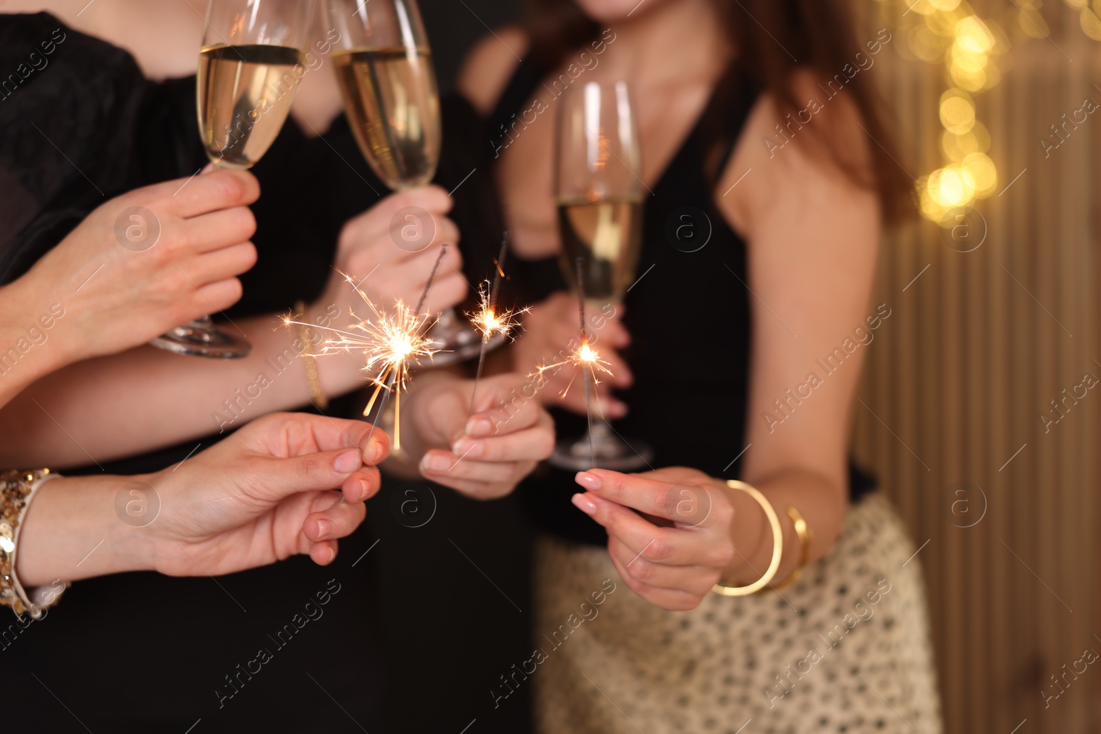 Photo of Women celebrating New Year with sparklers and wine glasses indoors, closeup