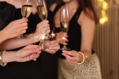 Photo of Women celebrating New Year with sparklers and wine glasses indoors, closeup