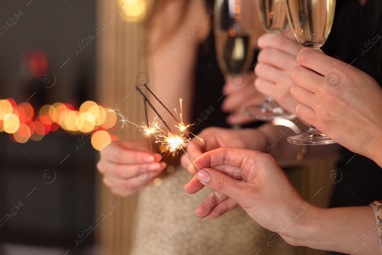 Photo of Women celebrating New Year with sparklers and wine glasses indoors, closeup