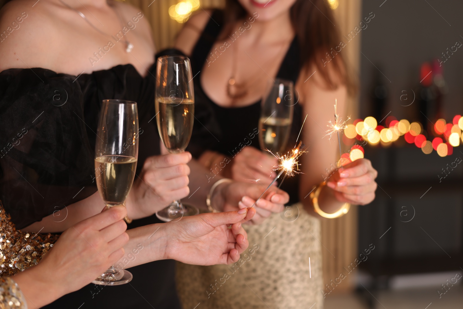 Photo of Women celebrating New Year with sparklers and wine glasses indoors, closeup