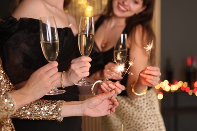 Photo of Women celebrating New Year with sparklers and wine glasses indoors, closeup