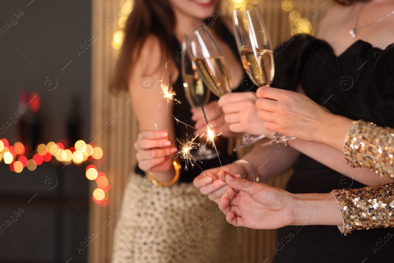 Photo of Women celebrating New Year with sparklers and wine glasses indoors, closeup