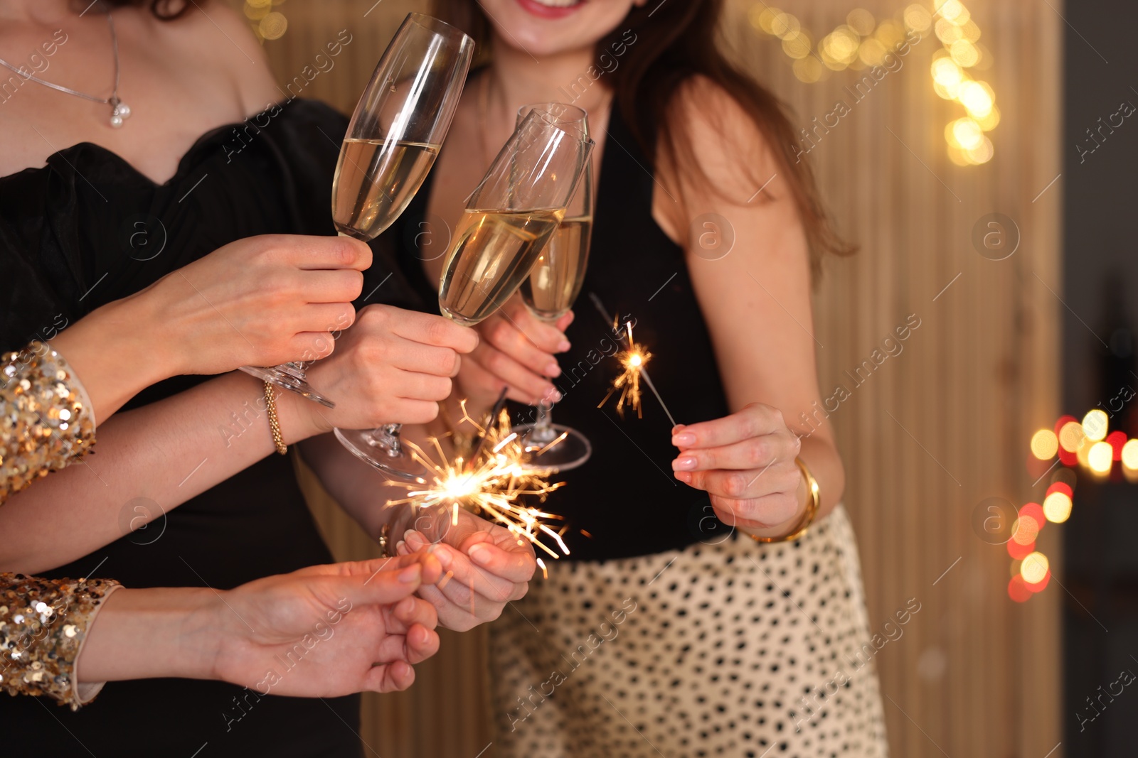 Photo of Women celebrating New Year with sparklers and wine glasses indoors, closeup