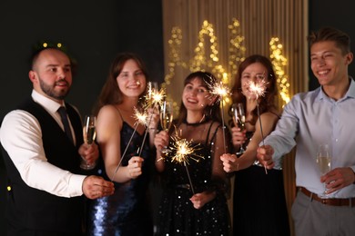 Photo of Friends celebrating New Year with sparklers and wine glasses indoors