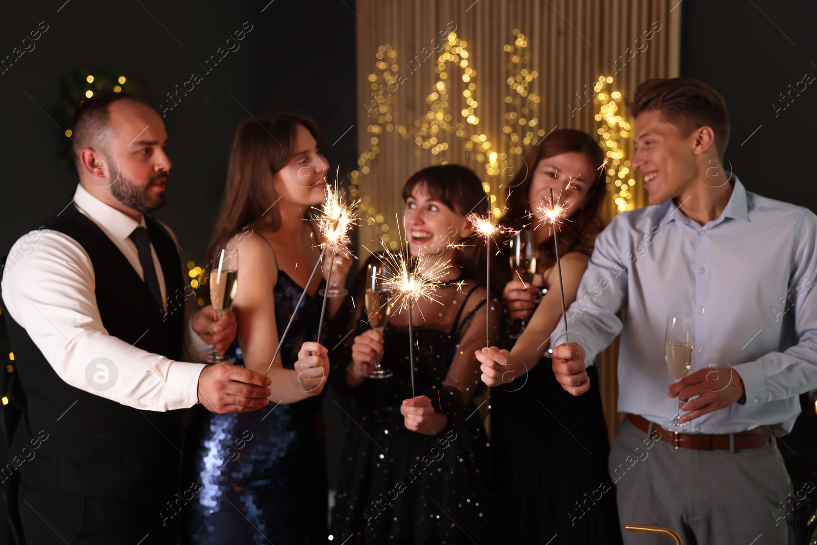 Photo of Friends celebrating New Year with sparklers and wine glasses indoors