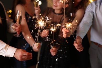 Photo of Friends celebrating New Year with sparklers and wine glasses indoors, closeup