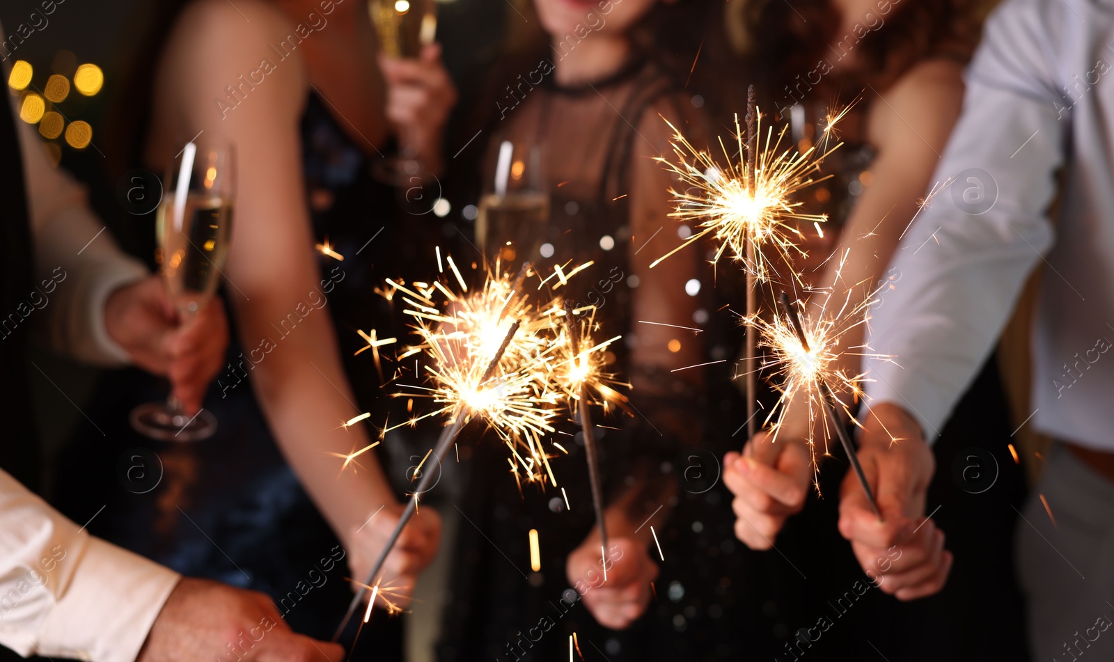 Photo of Friends celebrating New Year with sparklers and wine glasses indoors, closeup