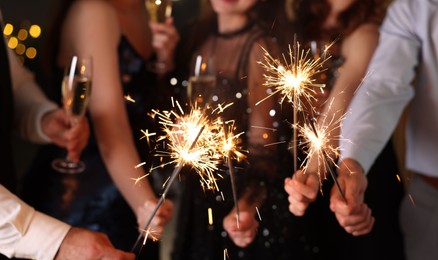 Photo of Friends celebrating New Year with sparklers and wine glasses indoors, closeup