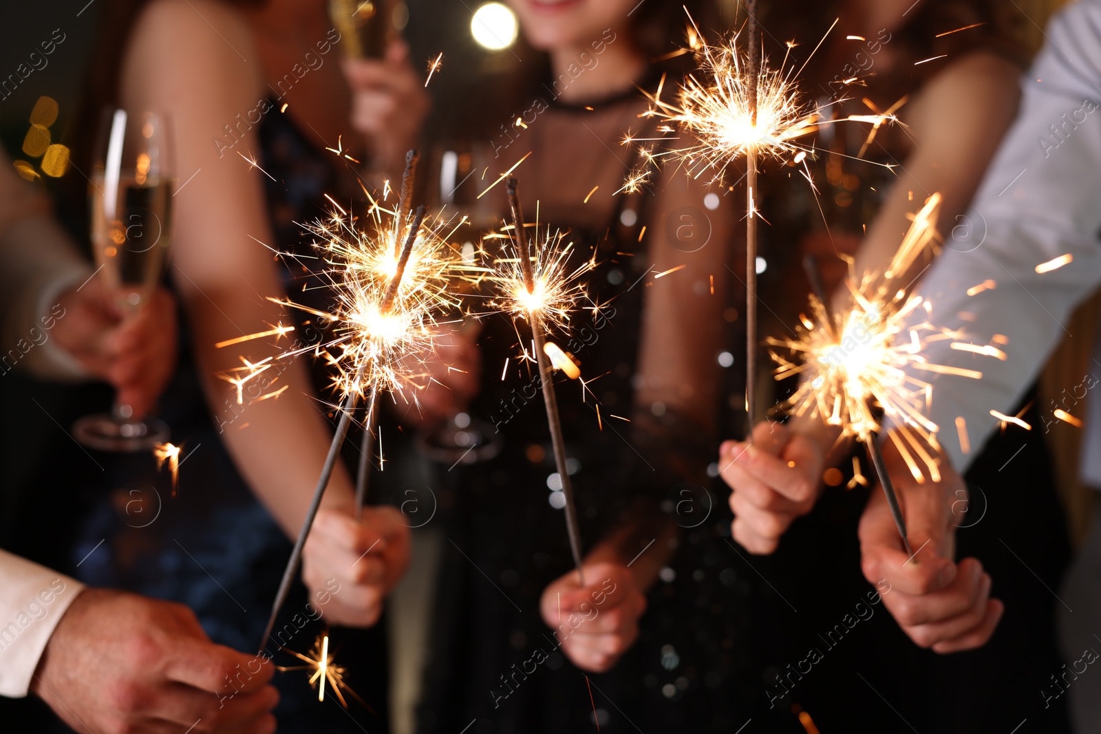 Photo of Friends celebrating New Year with sparklers and wine glasses indoors, closeup