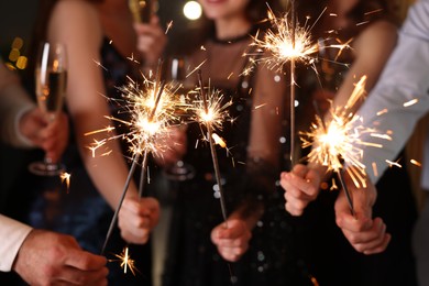 Photo of Friends celebrating New Year with sparklers and wine glasses indoors, closeup