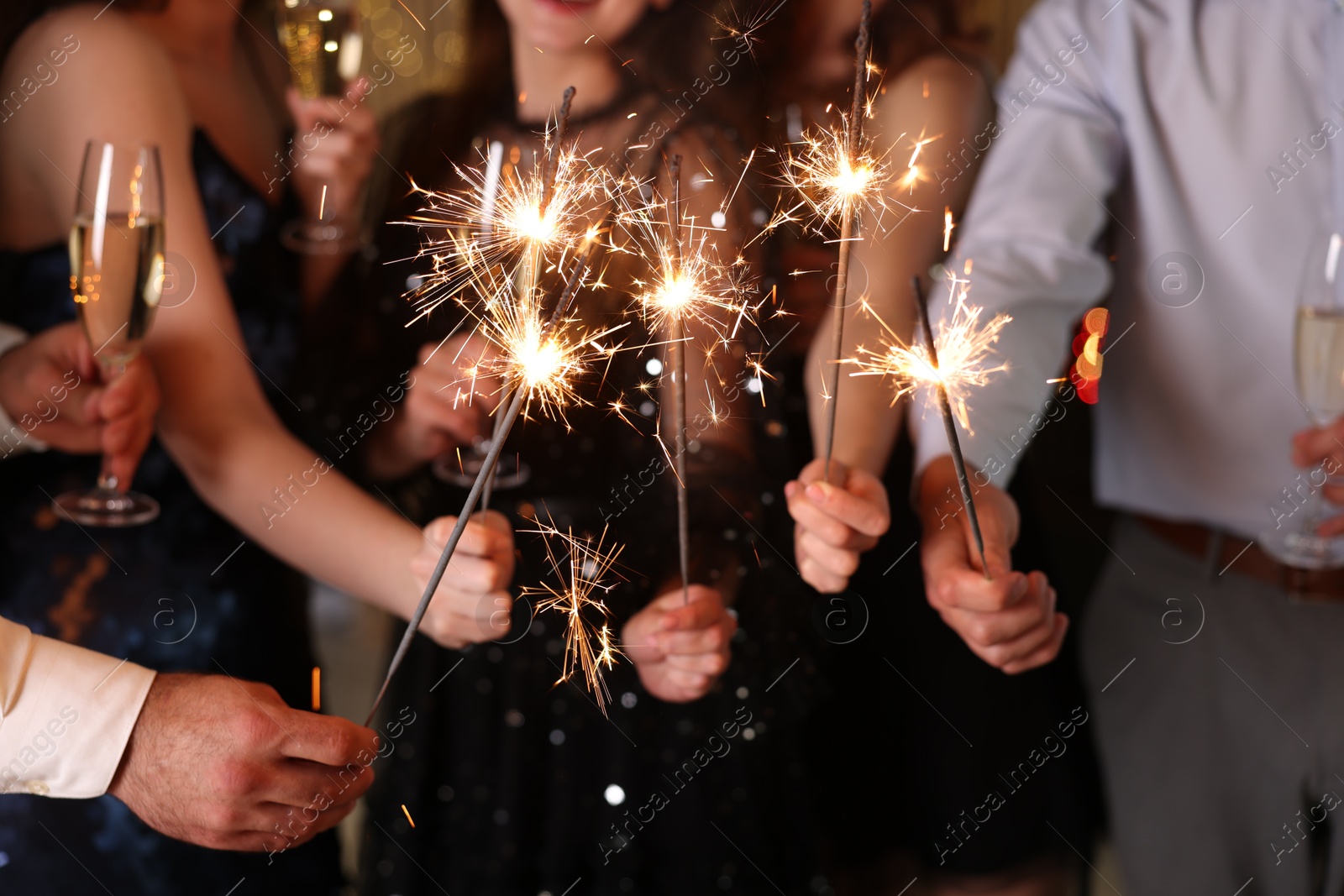 Photo of Friends celebrating New Year with sparklers and wine glasses indoors, closeup