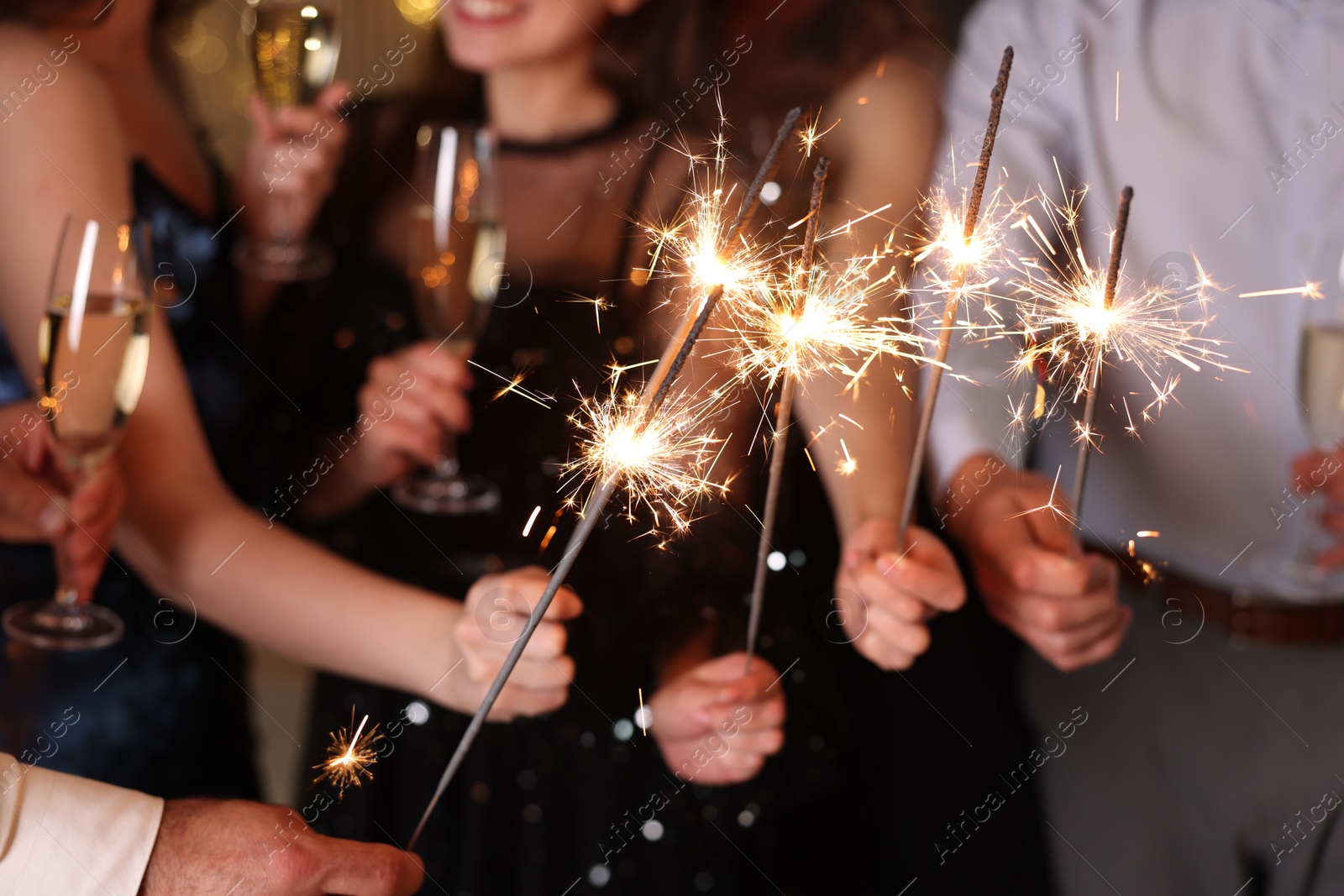 Photo of Friends celebrating New Year with sparklers and wine glasses indoors, closeup