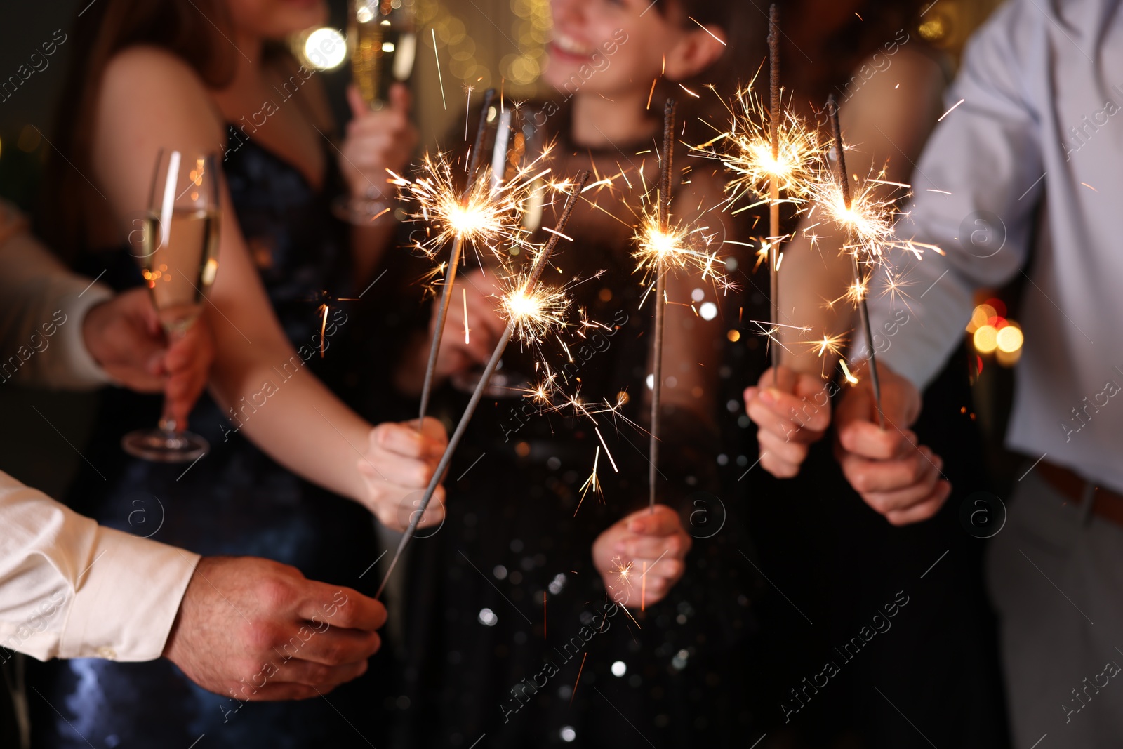 Photo of Friends celebrating New Year with sparklers and wine glasses indoors, closeup