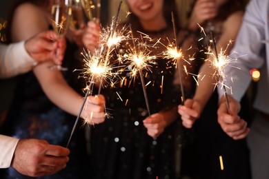 Photo of Friends celebrating New Year with sparklers and wine glasses indoors, closeup