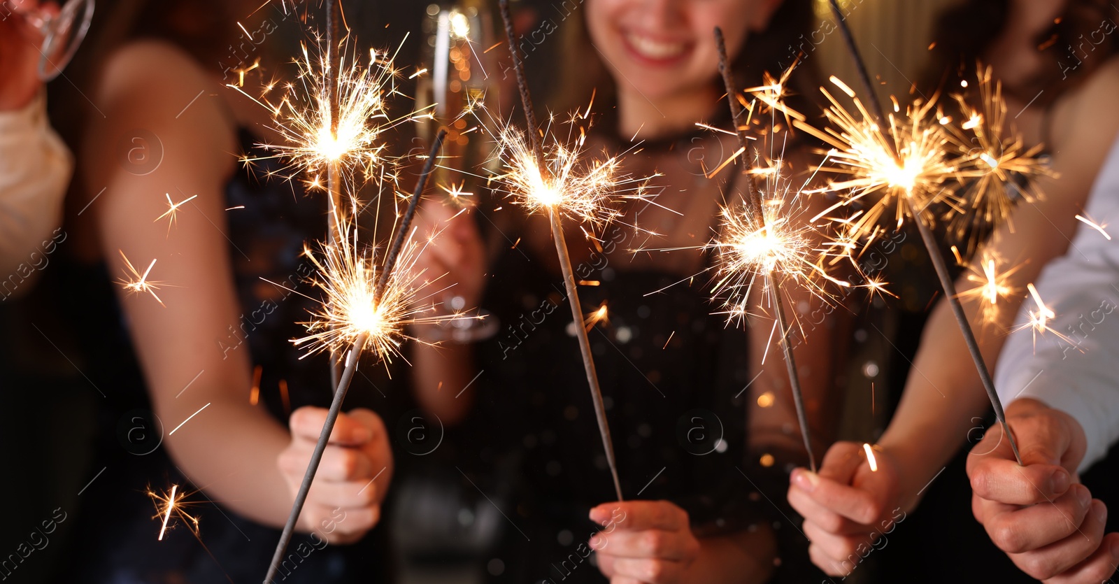 Photo of Friends celebrating New Year with sparklers and wine glasses indoors, closeup