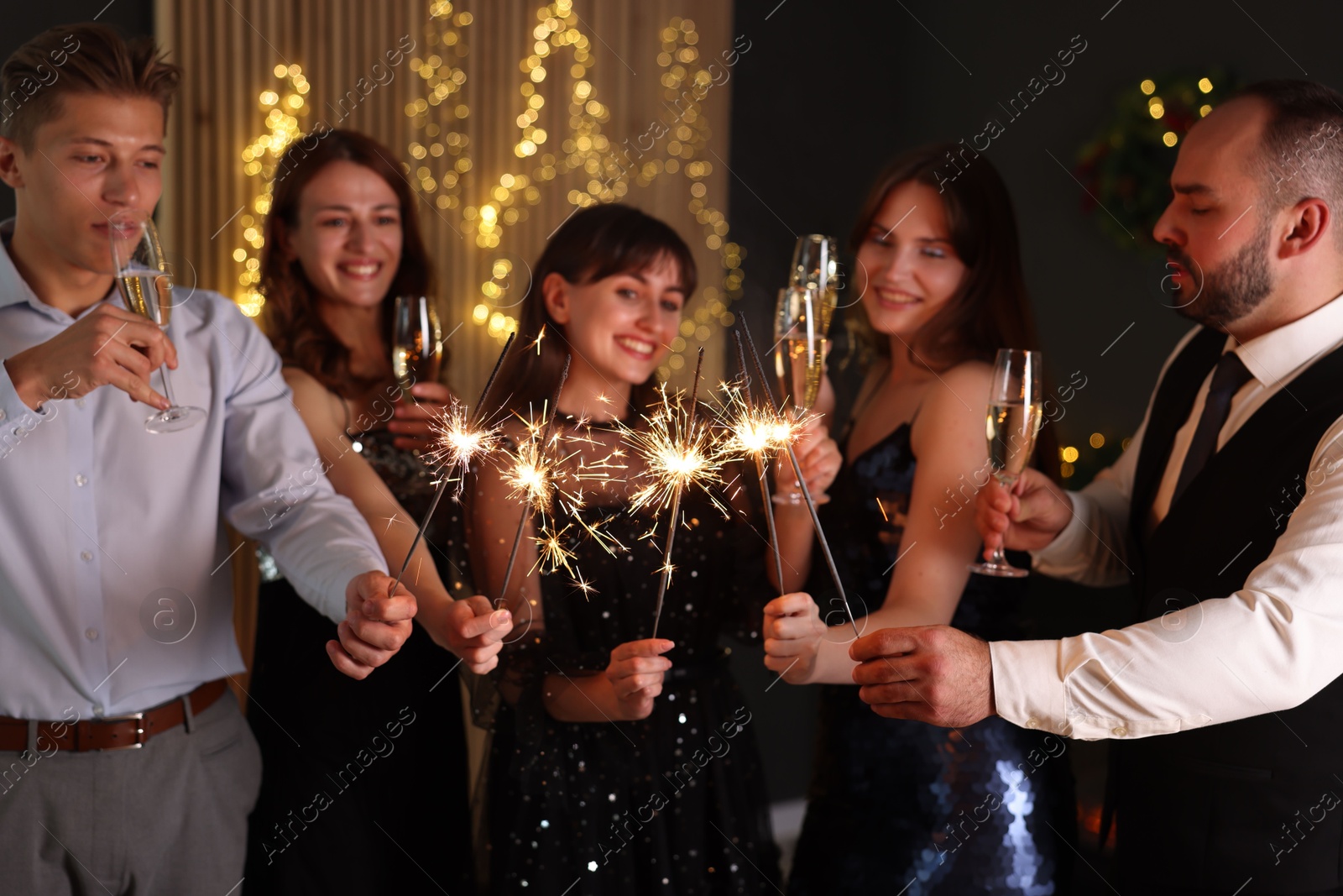 Photo of Friends celebrating New Year with sparklers and wine glasses indoors