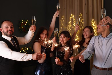 Photo of Friends celebrating New Year with sparklers and wine glasses indoors
