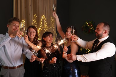 Photo of Friends celebrating New Year with sparklers and wine glasses indoors