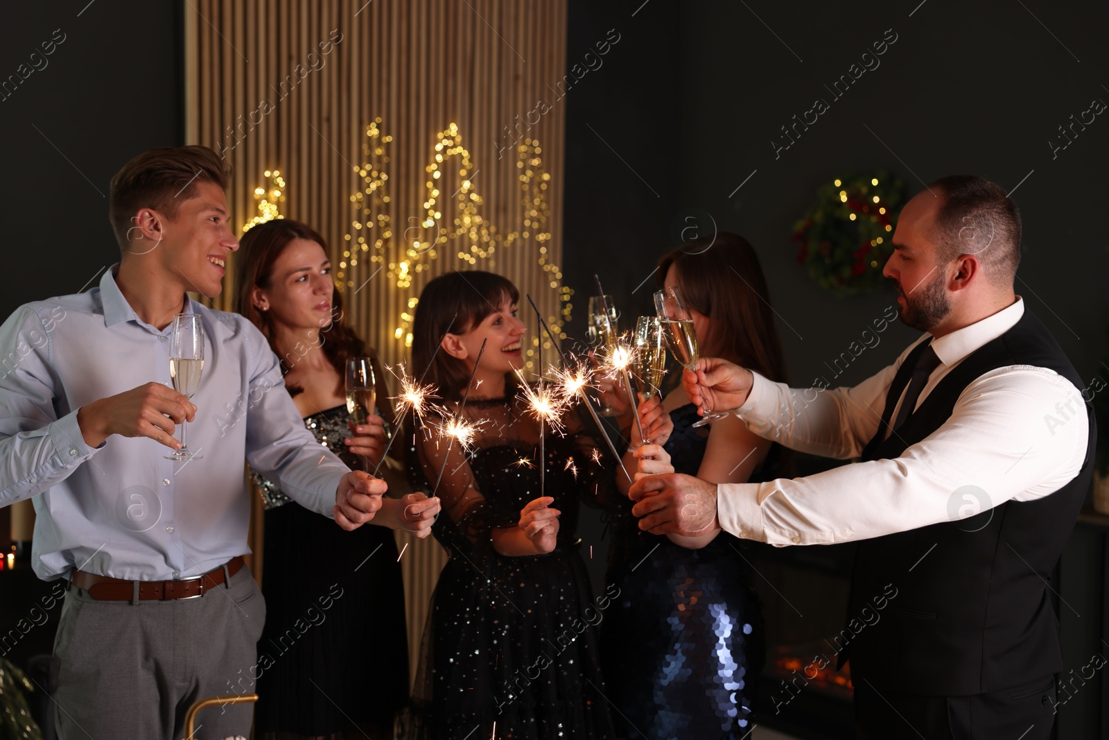 Photo of Friends celebrating New Year with sparklers and wine glasses indoors